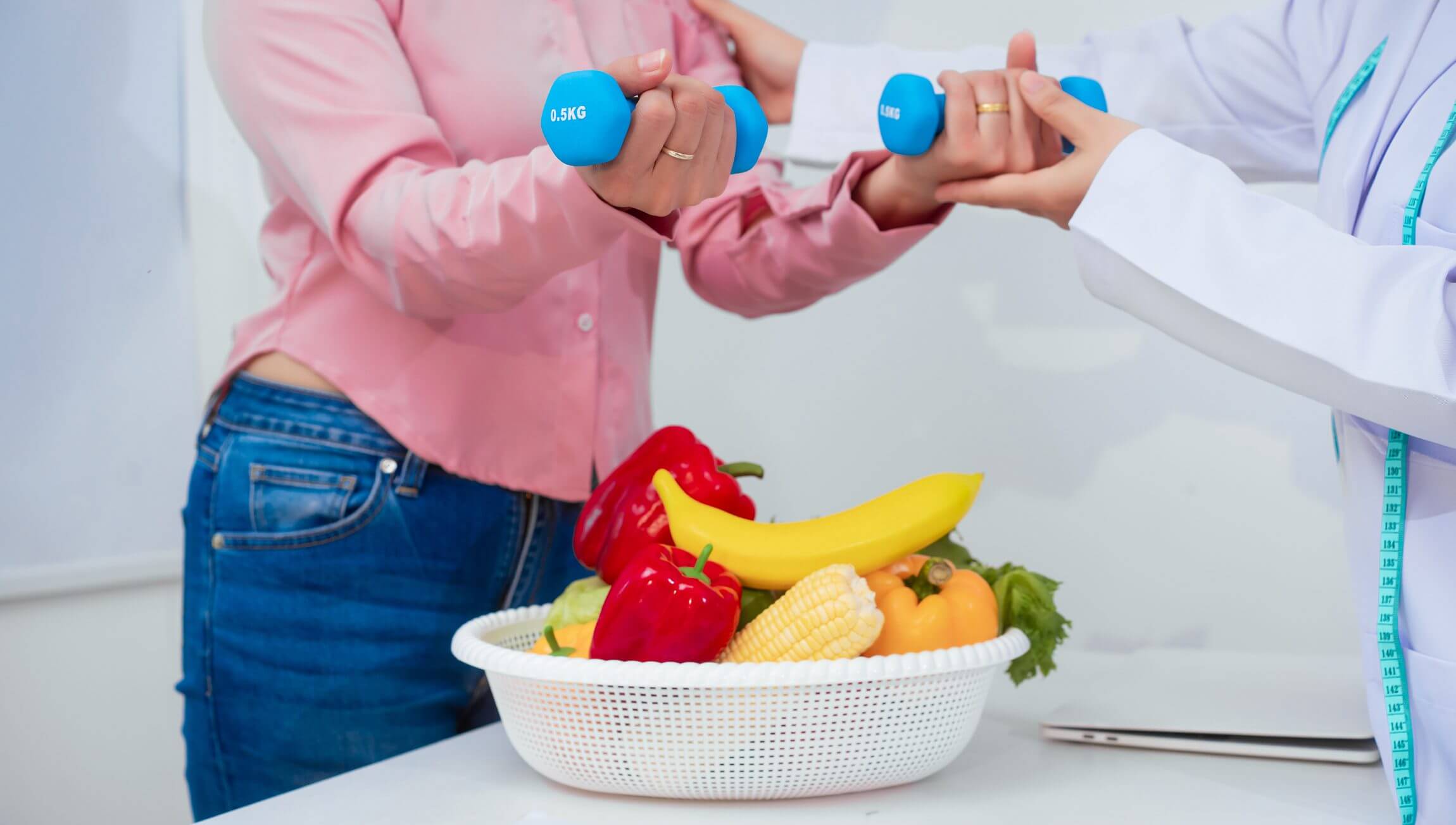 Person lifting blue dumbbells near a fruit basket.