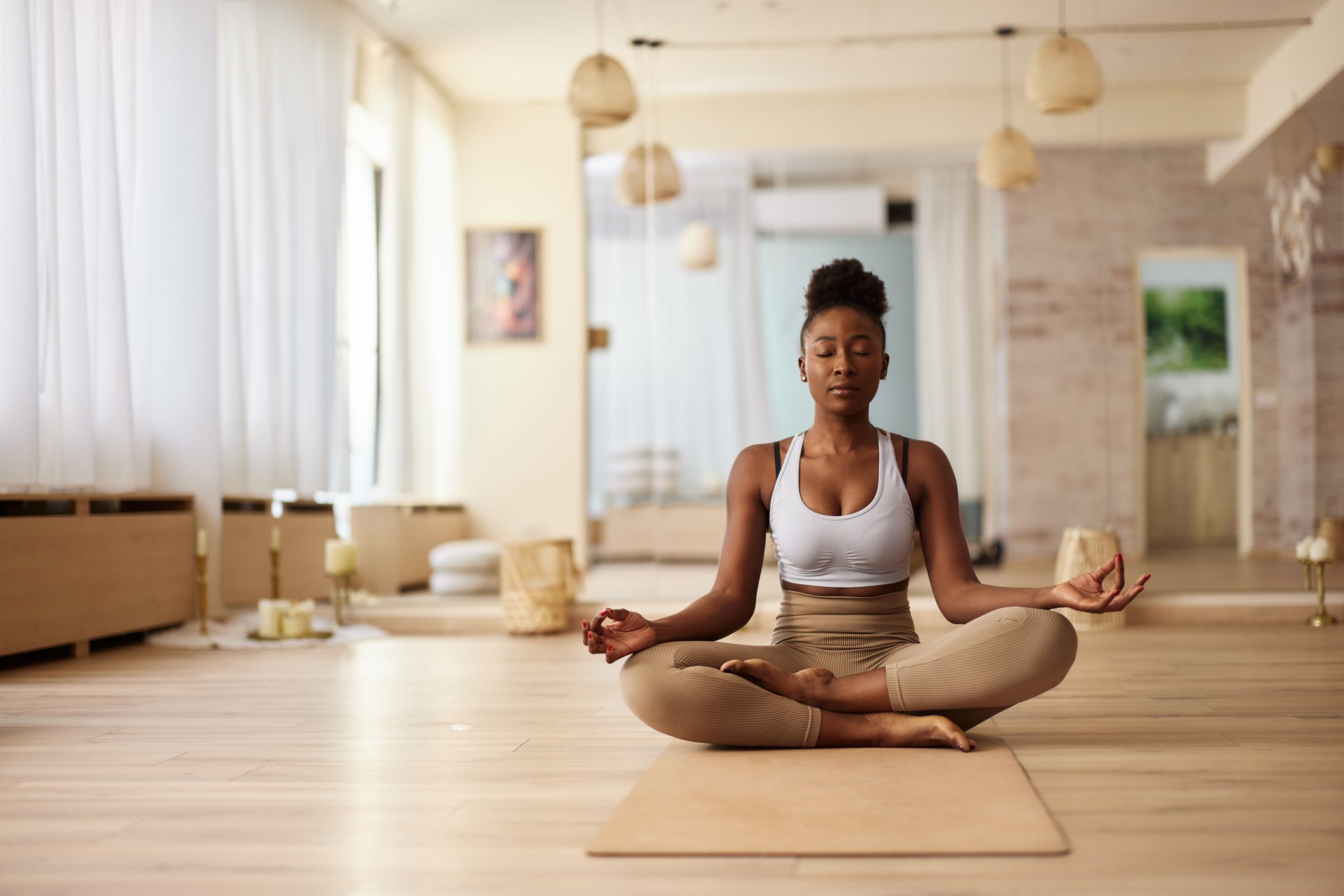 A woman meditating on a yoga mat in a bright, serene room.
