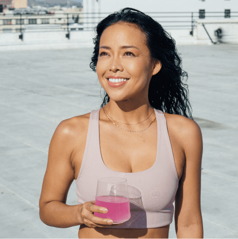 Smiling woman in sports bra holding pink drink